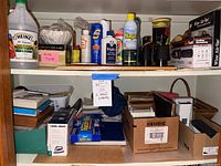 Shelf with cleaning supplies, vinegar, tape, note pads, boxed iron, and other items