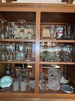 Glassware arranged in shelves including wine glasses, crystal jar with lid, votive holders, and mugs