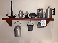 Shelf display of vintage metal kitchen decor items including candle holder with blue candle, syrup dispenser, teapot, small dish, and three hanging containers beneath the shelf.