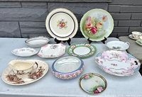 Wide view showing the full assortment of antique china plates and dishes with various floral designs and decorative rims.
