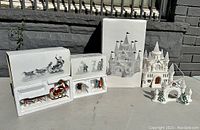 Photo showing ceramic light-up ice sculpture castle lamp and several accessory ceramic figurines displayed outside with original white boxes behind them.