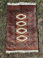 Full view of the Persian Yalameh wool rug laid on grass showing intricate geometric medallions and multiple patterned borders in traditional colors.