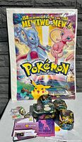 Overview photo showing the vintage Pokémon movie poster with Mewtwo and Mew, several Pokémon collectible card tins (including a large Snorlax tin), and other miscellaneous Pokémon trading card items.