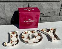 Photo of three bone china dishes spelling 'JOY' with original Royal Albert box placed behind them.