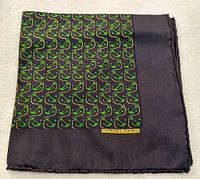 Folded view of black Hermes silk pocket square with green motif and Hermes Paris logo near edge.