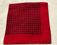 Close-up of folded red silk twill pocket square showing black checked pattern and Hermes-Paris logo