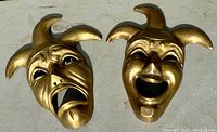 Photo of both brass Mardi Gras masks showing Comedy and Tragedy faces on concrete surface.