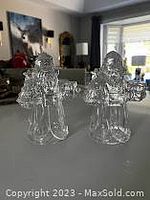 Two clear crystal Santa Claus shaped candle holders displayed together on a flat surface with a room background.