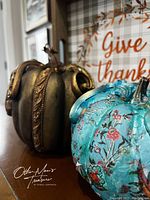 Side view close-up of the two decorative plastic pumpkins, bronze and turquoise, showing detailed painted designs.