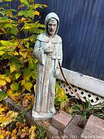 Concrete statue of Saint Francis of Assisi outdoors next to plants and bricks