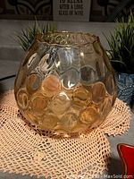 Round amber glass vase with raised bubble texture and wavy rim placed on a crocheted mat.