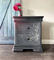 Front view of oversized nightstand painted grey with white floral design on lower drawer and black knobs.