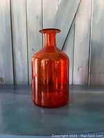 Photo of the large translucent orange glass bottle showing its cylindrical shape, narrow neck, and glossy finish.