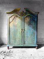 Front view of large double-door wooden cabinet with a carved top and decorative chalk paint finish in blue, green and purple tones.