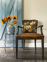 Full view of the brown painted wooden chair with floral design on the backrest next to a blue door and sunflower vase for staging