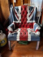 Front view of upholstered armchair with painted Union Jack pattern showing tufted upholstery and broken front leg.