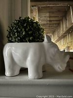 Side view of white ceramic rhino-shaped plant pot with artificial green foliage inside.