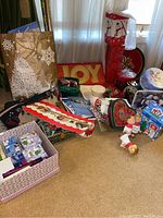 Overview of various Christmas-themed items: gift bags, cookie tins, trays, banners, and fabric decor items arranged on the floor and against a wall
