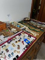 Wide view showing a variety of clip on earrings in several boxes and an arrangement of beaded necklaces laid out on a dresser