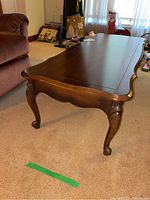 Front side view of the solid wood rectangular coffee table with curved curved legs on carpeted floor and drawer visible in the side panel.