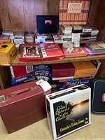 Two shelves of cabinet containing assorted board games and card games including multiple Trivial Pursuit sets, Ontario Trivia Challenge, box of dominos, Solo Bridge, and playing cards.