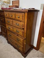 Full view of the wood highboy dresser showing 5 drawers, metal handles, and some surface wear. The dresser top has some small items placed on it.