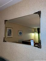 Photo showing the full mirror mounted on a wall with its gilded decorative corners and bevelled edge visible.
