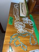 Photo showing several strands of freshwater pearl necklaces alongside a green stone necklace with a pendant and a jade stone necklace.