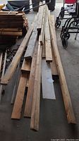 Pile of wooden boards mostly 2x4s, weathered and about 10 feet long, viewed from above in garage with other items nearby