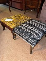 Two tapestry top foot stools side by side on carpet, one yellow floral, one black and white geometric
