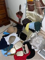 Photo showing variety of women's accessories on floor including hats, gloves, sunglasses and wallets as well as a vintage mirror, and clock.