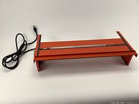 View of the strip heater showing orange metal frame, heating element, and attached power cord.