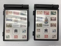 Two Canadian Centennial stamp sets in black plastic cases, displayed front-facing showing stamp sheets.
