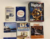 Five technical books on CNC machining, electronics, robotics, and CNC operations shown upright and stacked on a table.