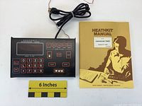 Front view of black HeathKit darkroom timer PT-1500 with digital display and buttons, wire connected. HeathKit manual beside it.