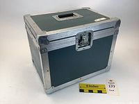 Angled external photo of greenish-gray rectangular case with aluminum frame and reinforced corners, showing top handle and latch.