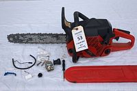 Jonsered CS2145 chainsaw with chain and bar, and spare parts spread out including a second carburetor, screws, spring, and other small parts.