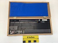 Open wooden case showing the interior lined with blue felt on the lid and black plastic compartments holding metal rods and tools