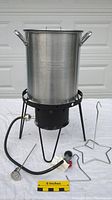 Full view of assembled propane burner with large aluminum pot, lid, and two turkey hooks on white surface