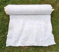 Rolled out section of white non-woven felt-like fabric showing texture and condition on grass.