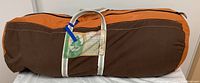 Brown and orange carrying case of the sleeping bag with a tag and handles.