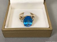 Front view of ring showing oval blue topaz and diamond shoulders in box