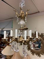 Front angled view of chandelier showing 8 brass arms with attached crystal prisms and white candle covers.