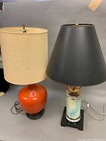 Two lamps side by side: orange ceramic base lamp with beige shade, and lucite/ceramic/brass lamp with black shade.