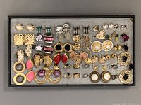 Full view of tray with multiple pairs of costume earrings arranged in rows.