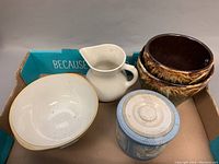 All five ceramic and pottery pieces in cardboard box: large planter pot, white pitcher, blue lidded jar, brown bowls, beige bowl.