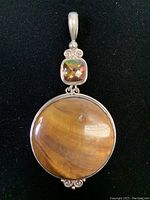 Front view of the 925 silver pendant with large round Tiger's Eye stone and smaller faceted square stone with silver scroll setting.