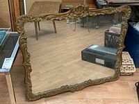 Full view of antique wall mirror showing ornate carved wooden frame and reflection of floor and nearby furniture.