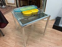 Side view of chrome frame and tinted glass top side table with the three serving trays placed on top
