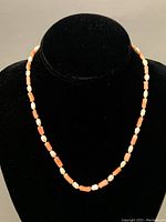 Full view of the necklace displayed on a black stand showing the alternating pattern of coral beads and freshwater pearls.